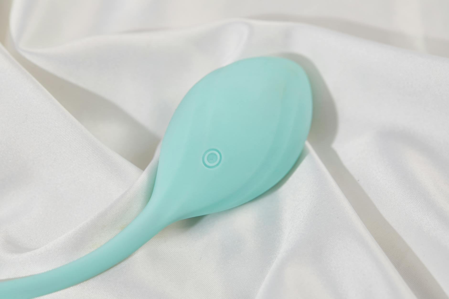 A teal lemon clitoral vibrator on soft white silk, symbolizing gentle healing and personal reclamation