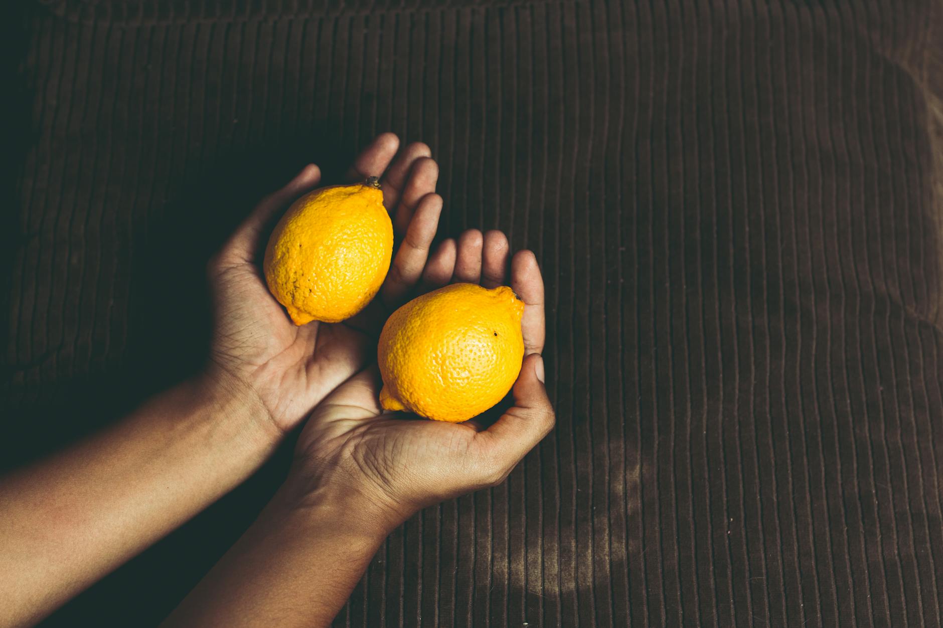 A hand holding a lemon-colored vibrator against a minimalistic purple backdrop, showcasing modern sensuality.