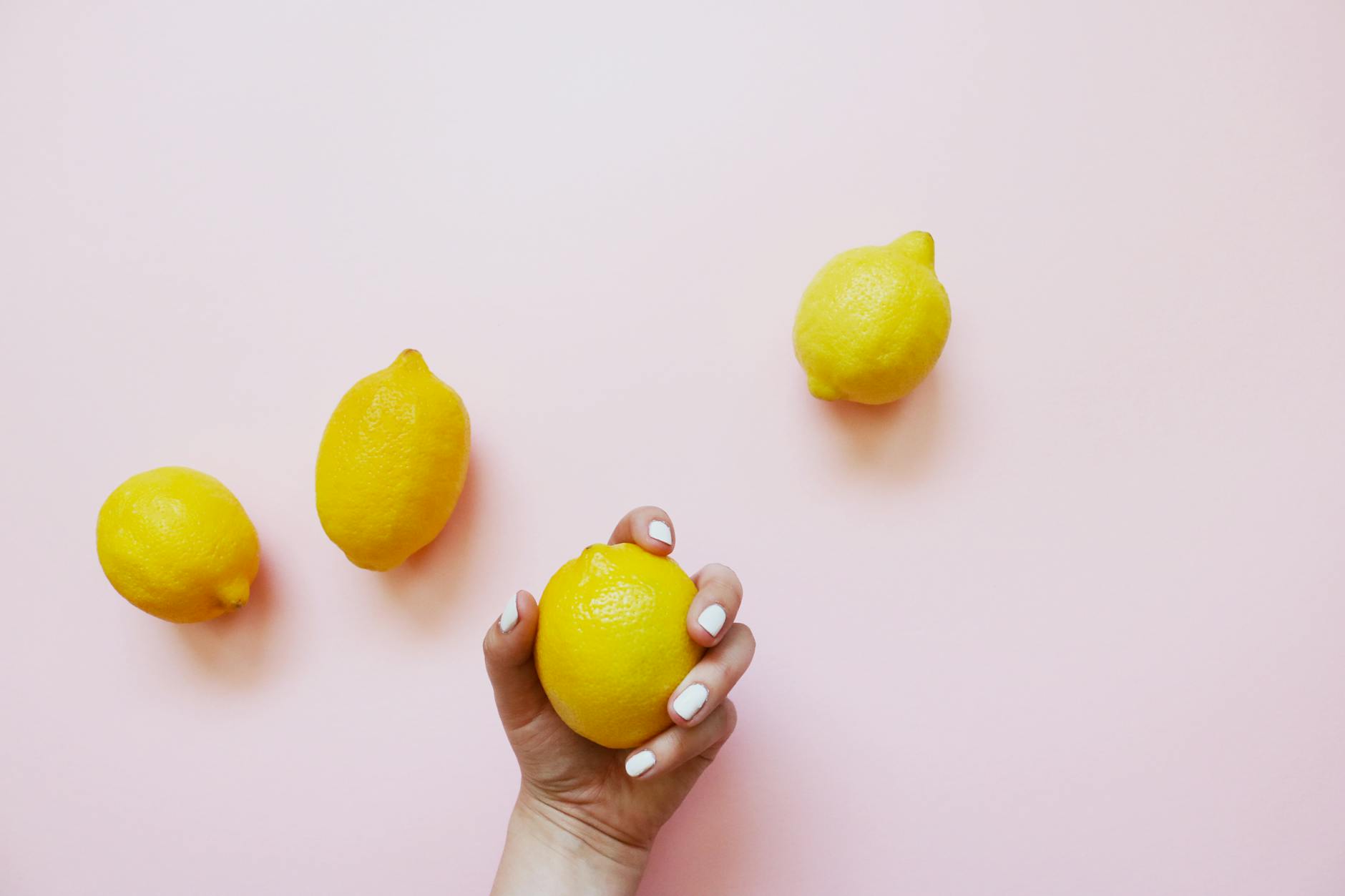 A hand holding a bright lemon on soft pink background, symbolizing fresh approaches to pleasure and wellness