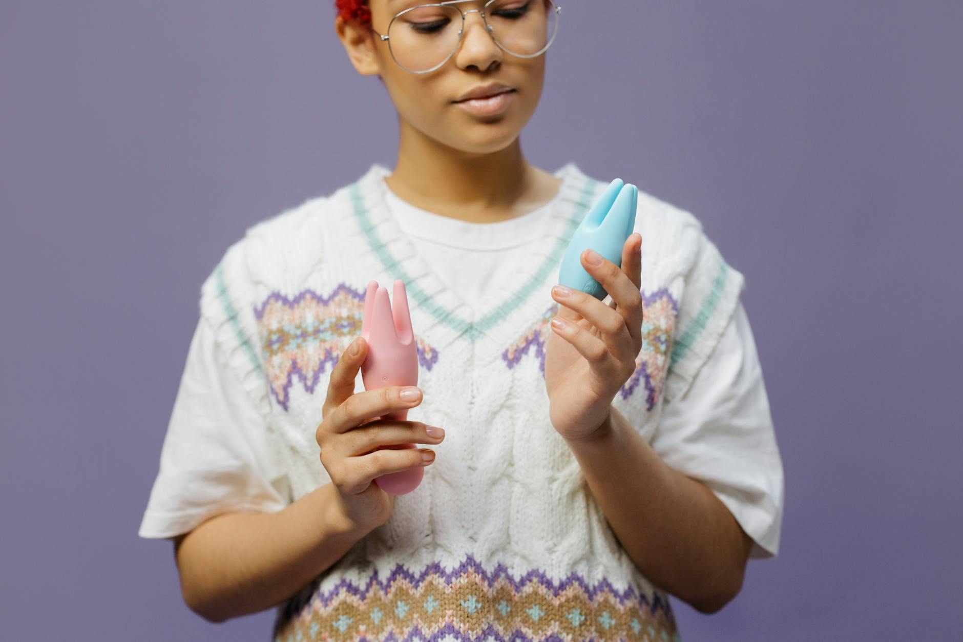 Woman holding various vibrators thoughtfully, considering clitoral sensitivity and recovery