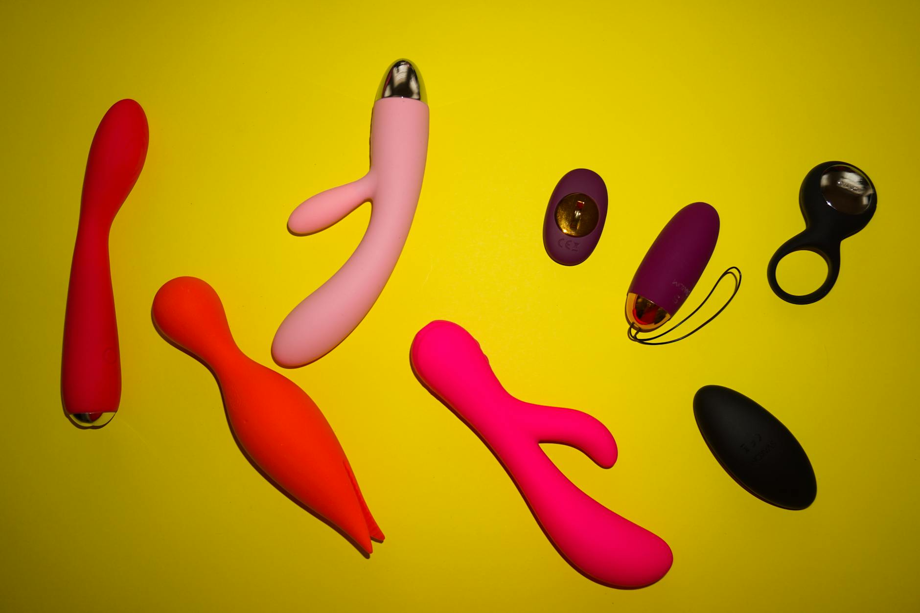 Vibrant collection of various colorful sex toys arranged on a bright yellow surface
