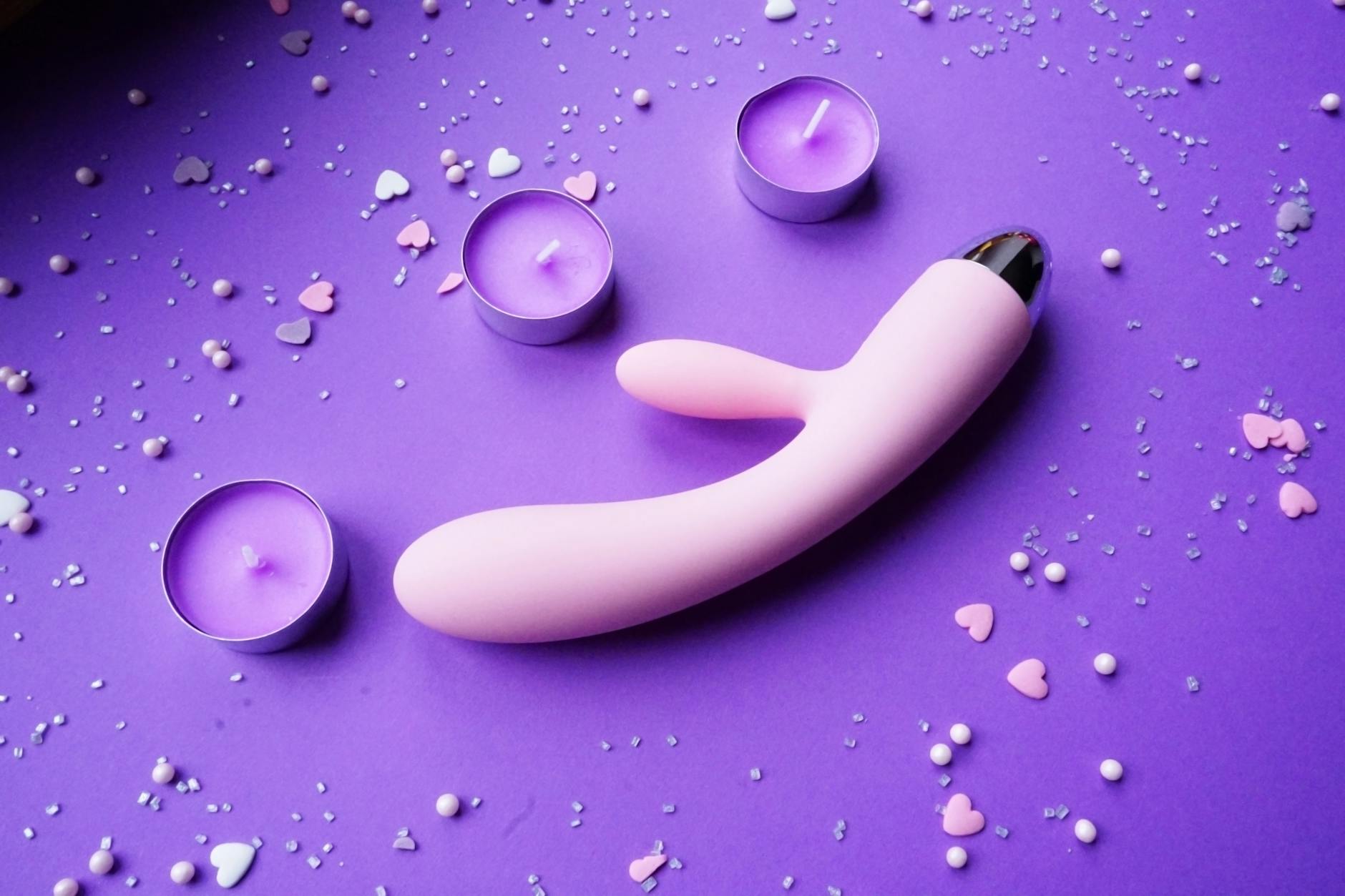 A pink vibrator surrounded by heart confetti and candles on a purple background, representing personalized pleasure choices.